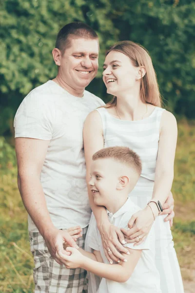 The family is in nature, mom hugs her son and dad hugs mom and everyone is smiling