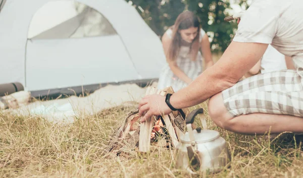 Family resting in nature with a tent mom prepares food on the background father lights a fire