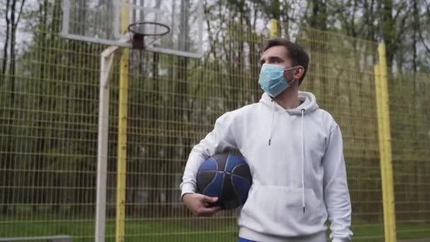 Muž sportovec basketbalista s míčem v masce v uzavřeném hřišti sám v karanténě během pandemie — Stock video