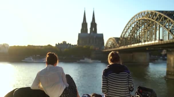 Deux touristes féminines s'assoient près du pont de Cologne par une journée ensoleillée. Allemagne — Video