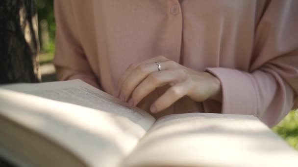 Девушка в розовой рубашке читает книгу в лесу солнечным утром, вид крупным планом — стоковое видео