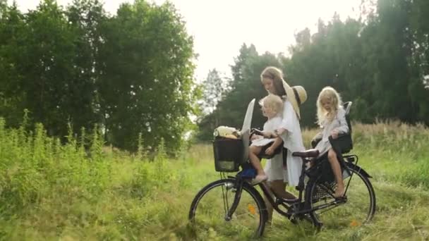 Young beautiful happy mother carries two children on a bicycle on the edge of the forest — Stock Video