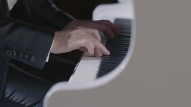 Siyah ceketli profesyonel bir virtüöz beyaz bir piyano çalar ve tuşları hızla çalar.