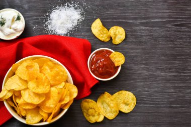 Kâsede çıtır patates cipsi ve ahşap bir masada peçeteyle soslar. Metin için yer.