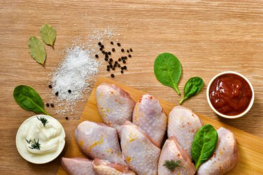 Kesme tahtasında çiğ tavuk bacağı, domates ve ahşap bir masada baharatlar. Yiyecek konsepti.