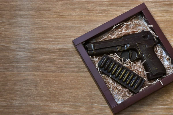 Chocolate in the form of a gun in a gift box on a wooden background. Place for text.