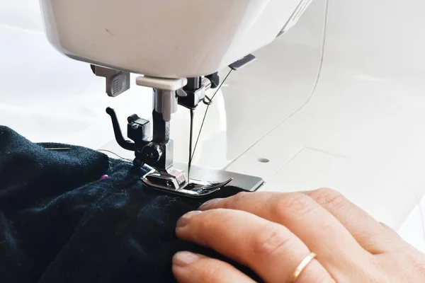 Sewing process.  Seamstress hands at work, threads and needles. Woman hands using the sewing machine to sew black blouse.