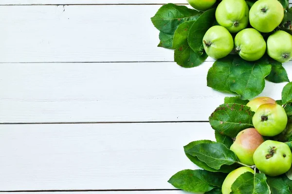 Fresh green apples with leaves on a white wooden background. Top view, copy space. Harvest concept.