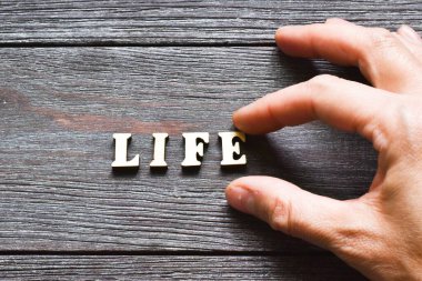 Ahşap bir arkaplanda hayat yazan tahta bir harfi tutan bir kadın. Güvenli bir hayat. Yaşamı koruyorum. Güvenli bir aile. Hayat hakkında. Boşluğu kopyala.