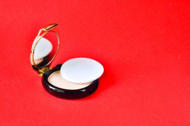 Kırmızı arka planda yuvarlak kutuda yüz pudrası. Moda kozmetik, doğal makyaj ürünü bileşimi. Temeli açık krem. Organik yüz pudrası, yanak kızartıcı.