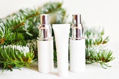 Köknar dallarında cilt bakımı kozmetik şişeleri. Tahta beyaz arka planda boş konteynırlar. Kadınlar için Noel hediyesi. Kış mevsimi kozmetik ürünleri. Boşluğu kopyala.