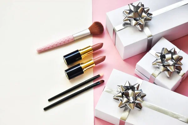 Makeup brush set and lipsticks, gifts boxes on a pink-white background. Concept beauty. Flat lay.