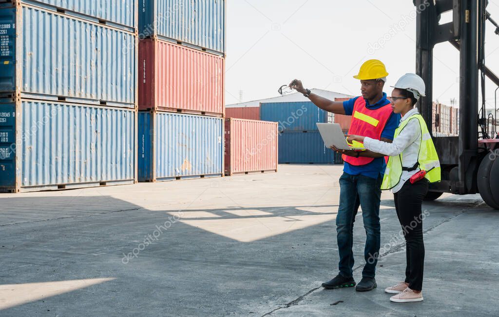 Two Black foreman man & woman worker working checking at Container cargo harbor holding laptop computer and using walkie-talkie to loading containers. African dock male and female staff business Logistics import export shipping concept.