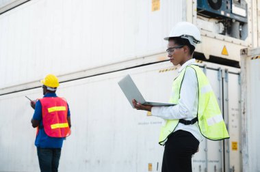 Konteyner kargo limanında dizüstü bilgisayarını kontrol eden ve konteynırları yüklemek için telsiz kullanan iki Kara Ustabaşı ve kadın işçi. Afrika rıhtımı erkek ve kadın personel lojistik ihracat nakliye konsepti.