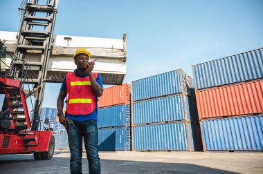 Kara ustabaşı konteynır kargo limanındaki vinç ve forklifti kontrol ediyor. Lojistik ihracat nakliye konsepti için telsiz telsiziyle Afrika rıhtımı erkek personeli.