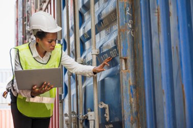 Kara ustabaşı kadın işçi konteynır kargo limanında kontrol ediyor dizüstü bilgisayarla konteynırları yüklüyor. Afrika rıhtımı kadın personel lojistik ithalat ihracat konsepti.