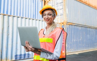 Ustabaşı kadın işçi konteyner kargo limanında kontrol ediyor dizüstü bilgisayarla konteynırları yüklüyor. Rıhtım kadın personel lojistik ithalat ihracat nakliye kavramı.