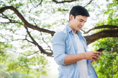 Genç beyaz iş adamı, parkta yürürken akıllı telefon kullanıyor..