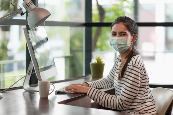 Beautiful asian woman wearing protection mask work from home in the morning. Young asian female working with computer stay at home.