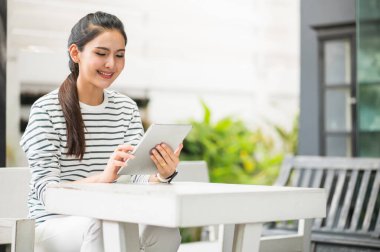 Tablet kullanan Asyalı kadın. Gülümseyen güzel kadın evde oturuyor ve çalışıyor..