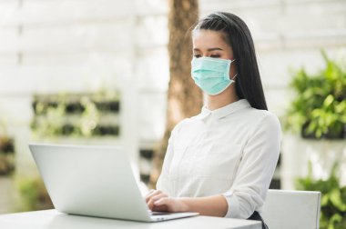 Güzel Asyalı kadın sabahları koruyucu maske takıyor. Dizüstü bilgisayarı olan genç Asyalı kadın evde kalıyor..