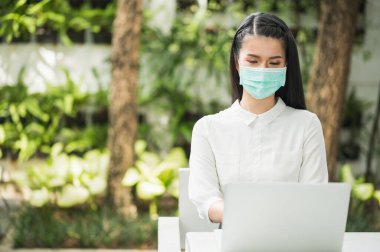 Güzel Asyalı kadın sabahları koruyucu maske takıyor. Dizüstü bilgisayarı olan genç Asyalı kadın evde kalıyor..