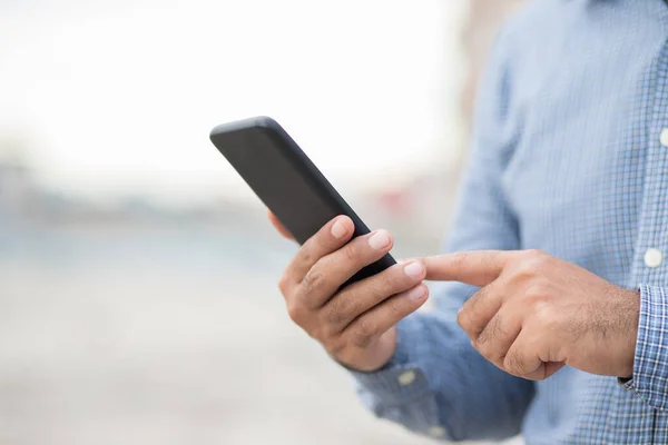 Şehrin arka planında siyah akıllı telefon kullanarak erkek elini kapat.