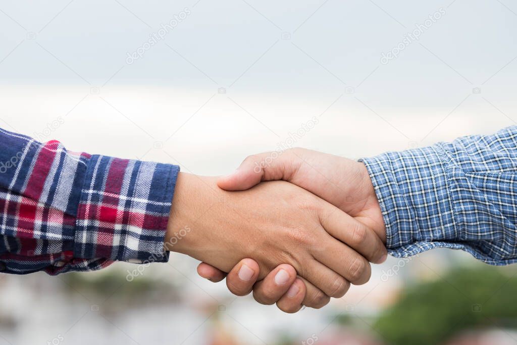 Two men shaking hands to dealing success agreement business. Business people wearing scott shirt on city view background.
