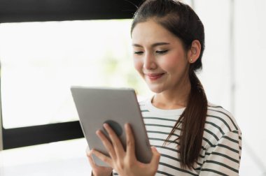 Tablet kullanan Asyalı kadın. Gülümseyen güzel kadın evde oturuyor ve çalışıyor..