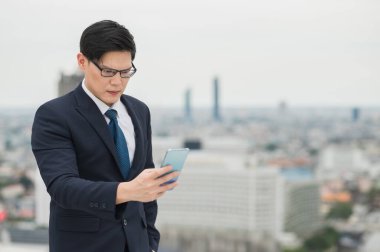 Genç Asyalı işadamı akıllı telefonu şehir geçmişi ile ilgili çalışmalarına metni bağlamak veya okumak için kullanıyor.