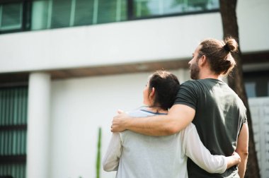 Koca ve hamile eş, evin önünde durmuş ve mutlu görünüyorlar. Sigorta ev aile kavramı.