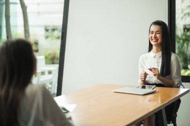 Güzel iki kadın yan yana oturup dizüstü bilgisayar ve tabletle masaya sosyal uzaklık kavramını tartışıyor..