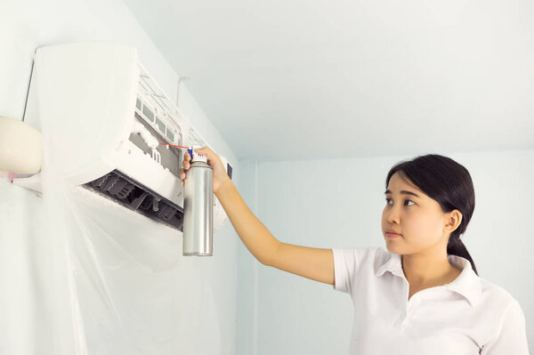 Woman cleaning air conditioner by foam cleaning agent.