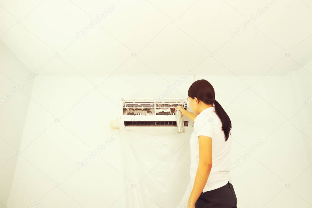 Woman checking and cleaning air conditioner inside room.