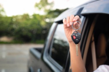 Araba anahtarlarını tutarken el kapama, araba mülkiyetini sembolize etme, otomobil satışı, kullanılmış araba galerisi, kiralama servisi, seyahat özgürlüğü ve açık yol kavramı.