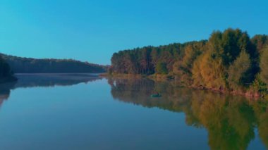 Teknede yalnız bir balıkçı. Sonbahar gölü şafağının ortasında balıkçı teknesi