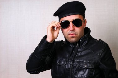 Siyah deri ceketli havalı rockçı stüdyodaki bulanık arka plan duvarında güneş gözlüğünü düzeltiyor. Özgüven duygusu.