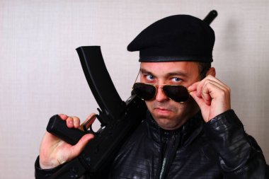 Siyah deri ceketli, saldırı tüfekli genç adam.