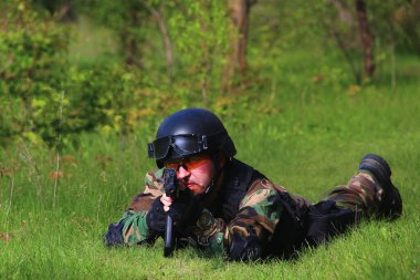 Keskin nişancı, ormandaki yeşil çimlerin üzerinde ateş ederek ağaçların dallarını koruyor..