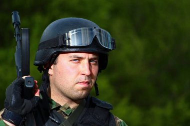 Askeri müteahhit askerle yüzleş. Kafasında miğfer olan, doğanın bulanık geçmişine sahip bir silahla yakın plan asker..