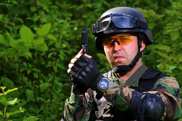 A special forces soldier with a helmet on his head holding a gun in his hands on a bright sunny day in the forest.