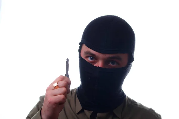 A man in a mask in the role of car thief or a house thief shows a key on a white background. Concept of theft
