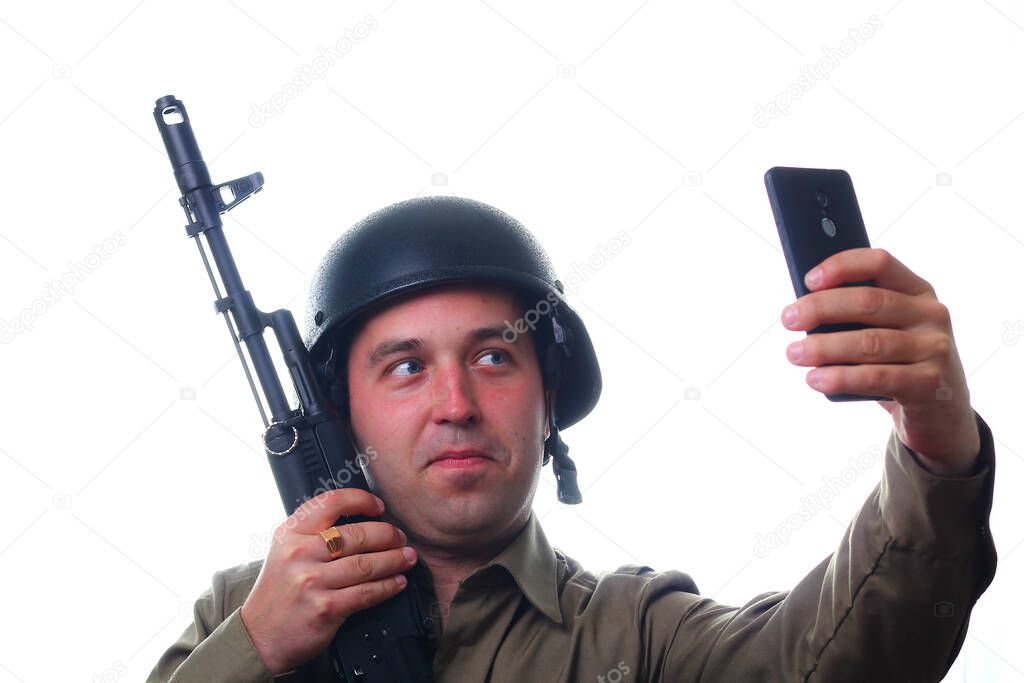 A man makes selfie in a military helmet with a rifle in his hands on a white background