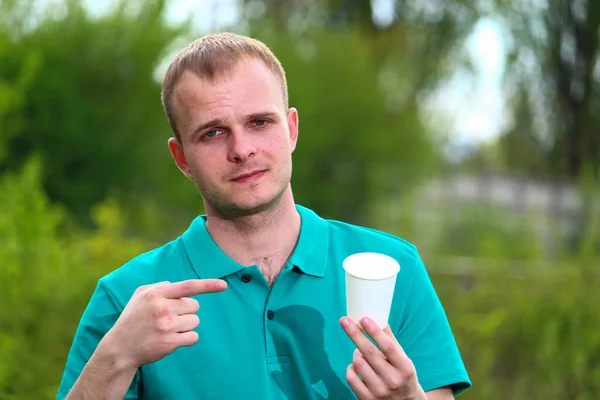 一位身穿绿色T恤的志愿者把他的手指放在一次性纸杯上 野餐的正确生态选择的概念 — 图库照片