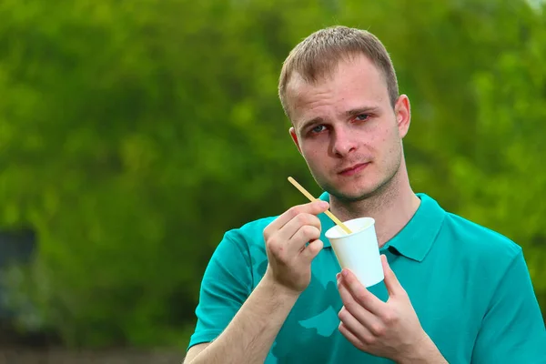 身穿绿色马夫T恤的志愿者手里拿着一个环保的一次性茶杯 用木勺展示野餐的正确选择 — 图库照片