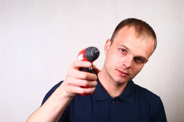 A worker in a classic blue t-shirt with a collar holds a professional electric screwdriver in his hand. Emotion of a call or response