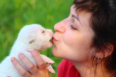Kadın bulanık arka planda beyaz bir köpek yavrusunu öpüyor, yakın plan.