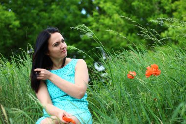 Güzel, genç esmer, yabani gelinciklerle bir çayırda dinleniyor.