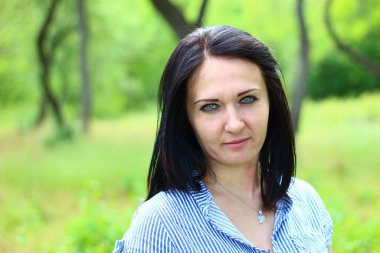 Güneşli bir günde yeşil ağaçların bulanık arka planında güzel, genç bir esmer.