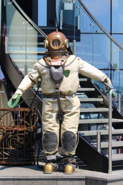 Üç cıvatalı dalış kıyafeti giymiş manken liman şehrinin deniz kenarındaki caddede.